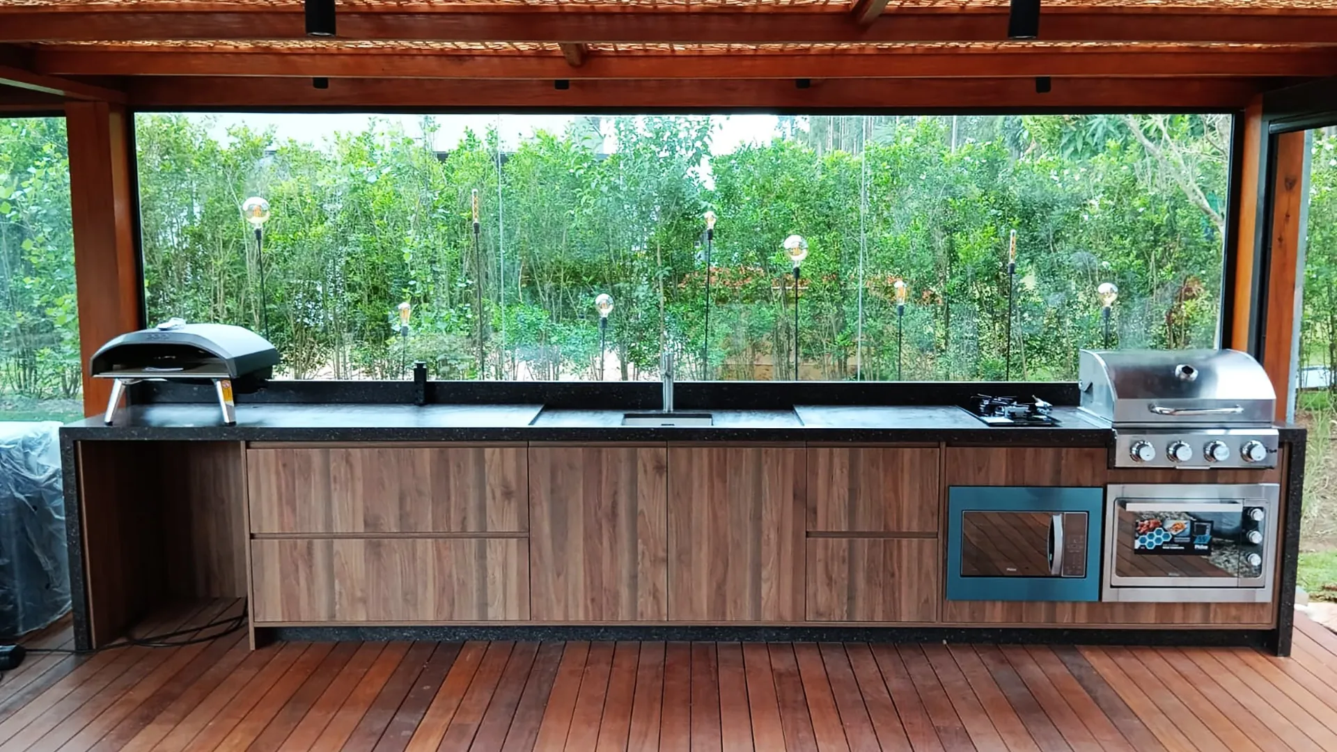Área gourmet com bancada em pedra natural e vista para o jardim